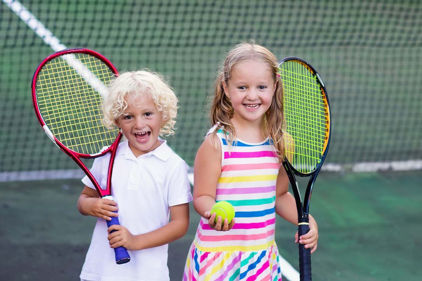Boy and girl playing tennis on outdoor court. Kids with tennis racket and ball in sport club. Active exercise. Summer activities for children. Training for young kid. Child learning to play.